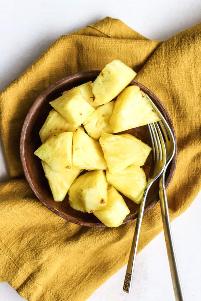 Fresh pineapple chunks on small wooden plate with two forks on gold linen, after using our favorite "how to cut a pineapple" method