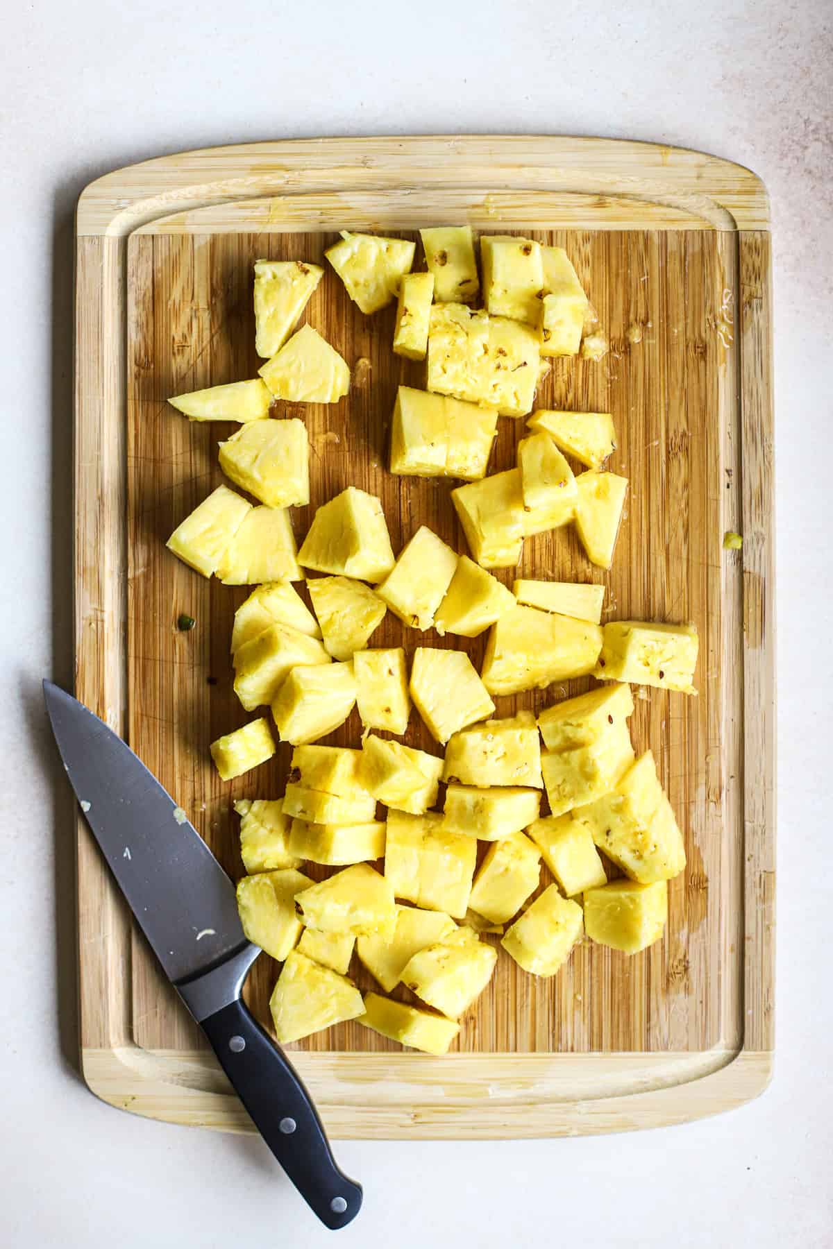 Fresh pineapple chunks on bamboo cutting board next to chef's knife