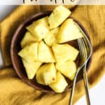 Fresh pineapple chunks on small wooden plate with two forks on gold linen, after using our favorite "how to cut a pineapple" method