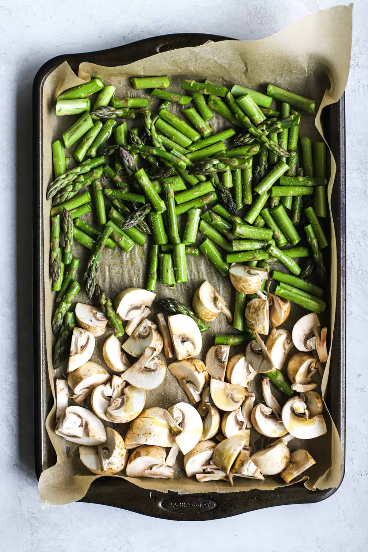 Chopped mushrooms and asparagus in olive oil and salt on parchment-lined sheet pan