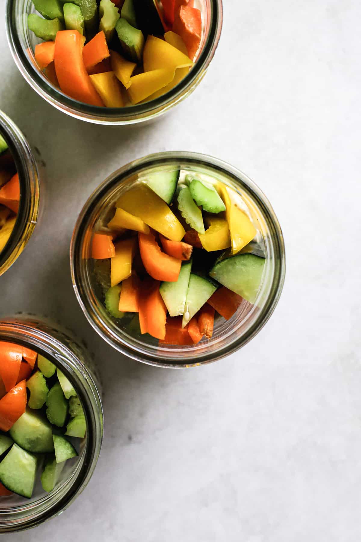 Four hummus and veggie jars on gray and white surface