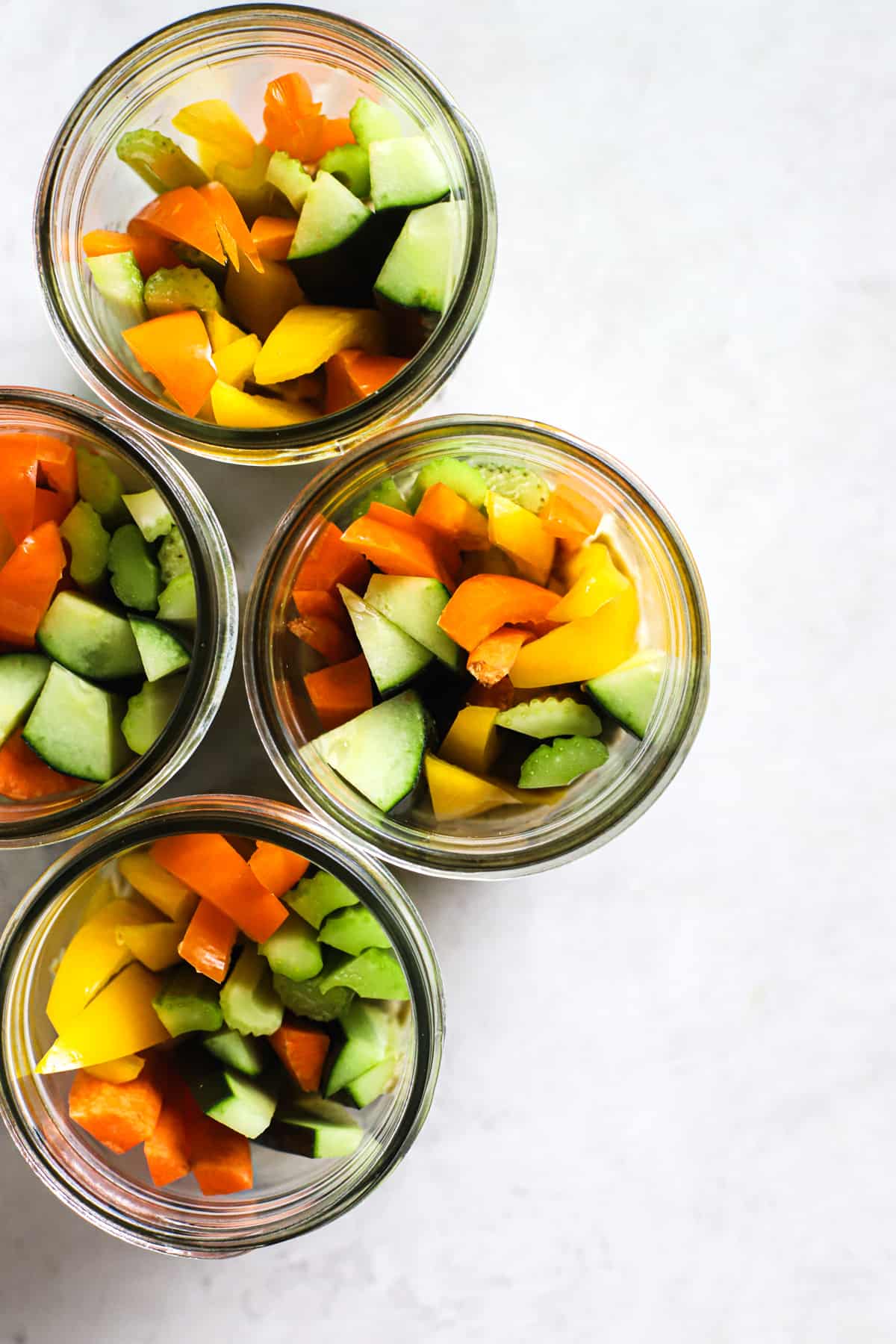 Four hummus and veggie jars on gray and white surface