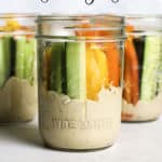 Three hummus and veggie jars on gray and white surface