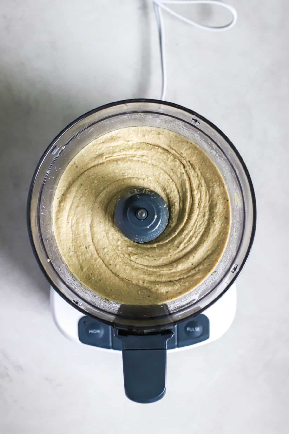 Lemon dill hummus ingredients blended together in food processor before adding ice water to smooth it out.