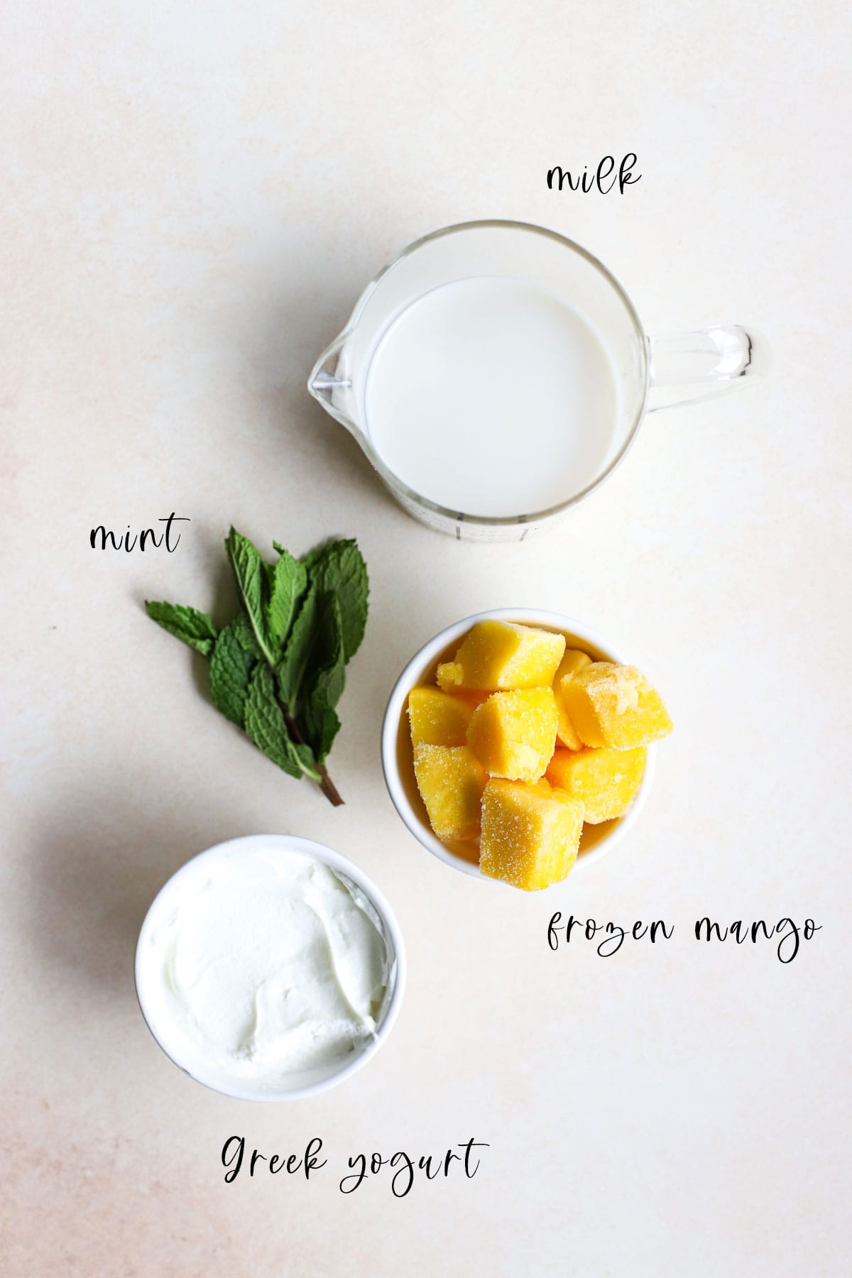 Frozen mango, Greek yogurt, fresh mint, and milk on beige and white gray surface