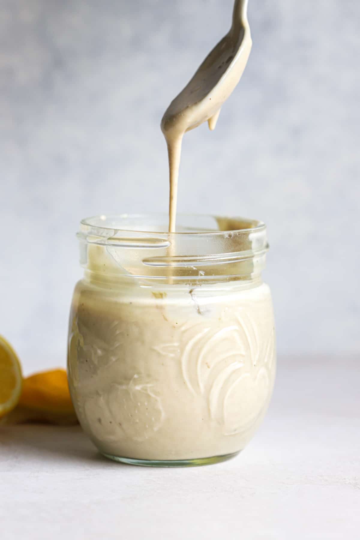 Tahini sauce dripping off of spoon into small glass jar.