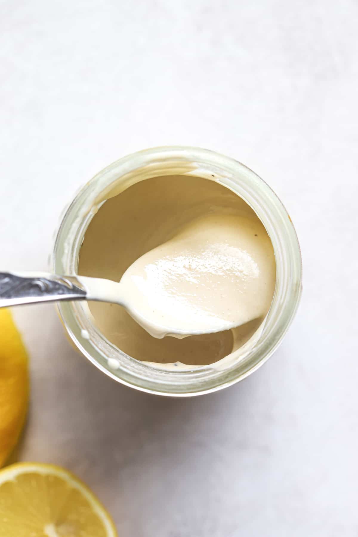 Tahini sauce in small glass jar with spoon and lemons on the side.