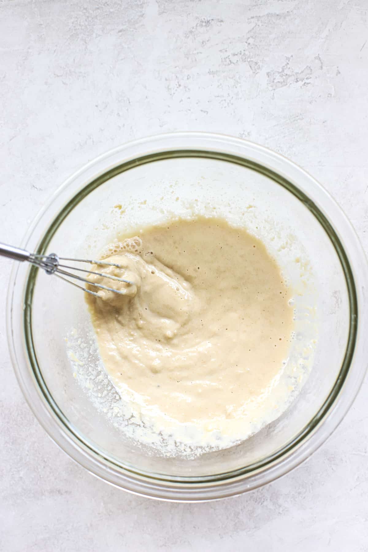 Tahini sauce being whisked together in clear glass bowl with mini whisk on gray and white surface.