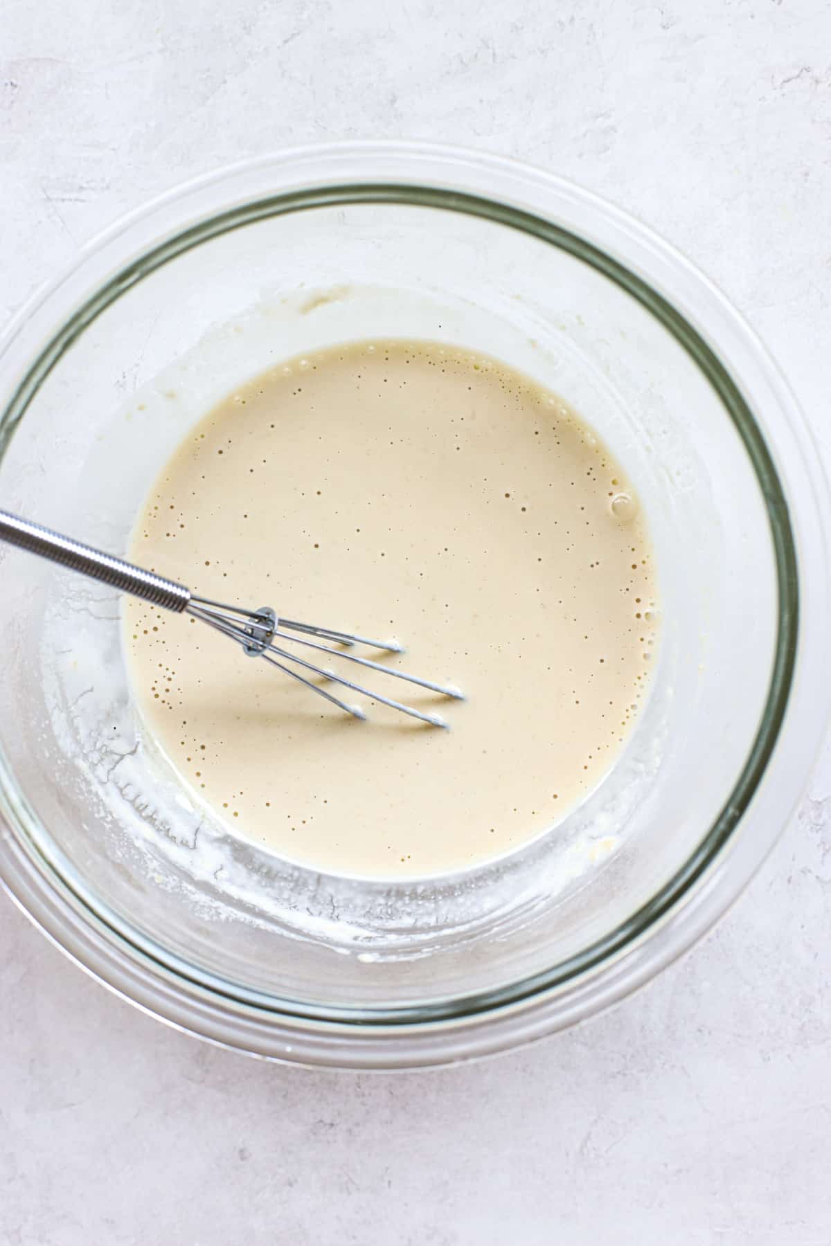 Tahini sauce completely whisked until smooth, in clear glass bowl on white and gray surface.