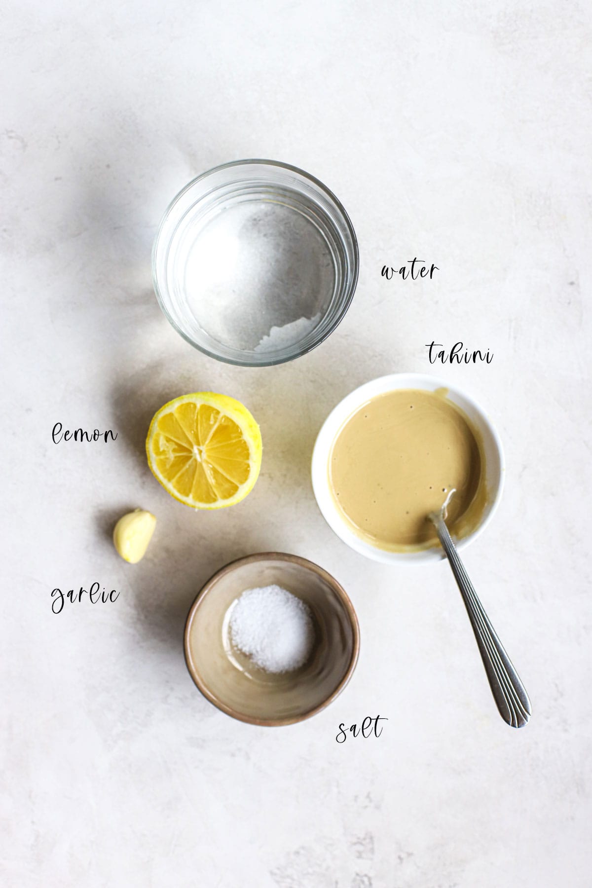 Water, tahini, lemon, garlic, and salt on white and gray surface.