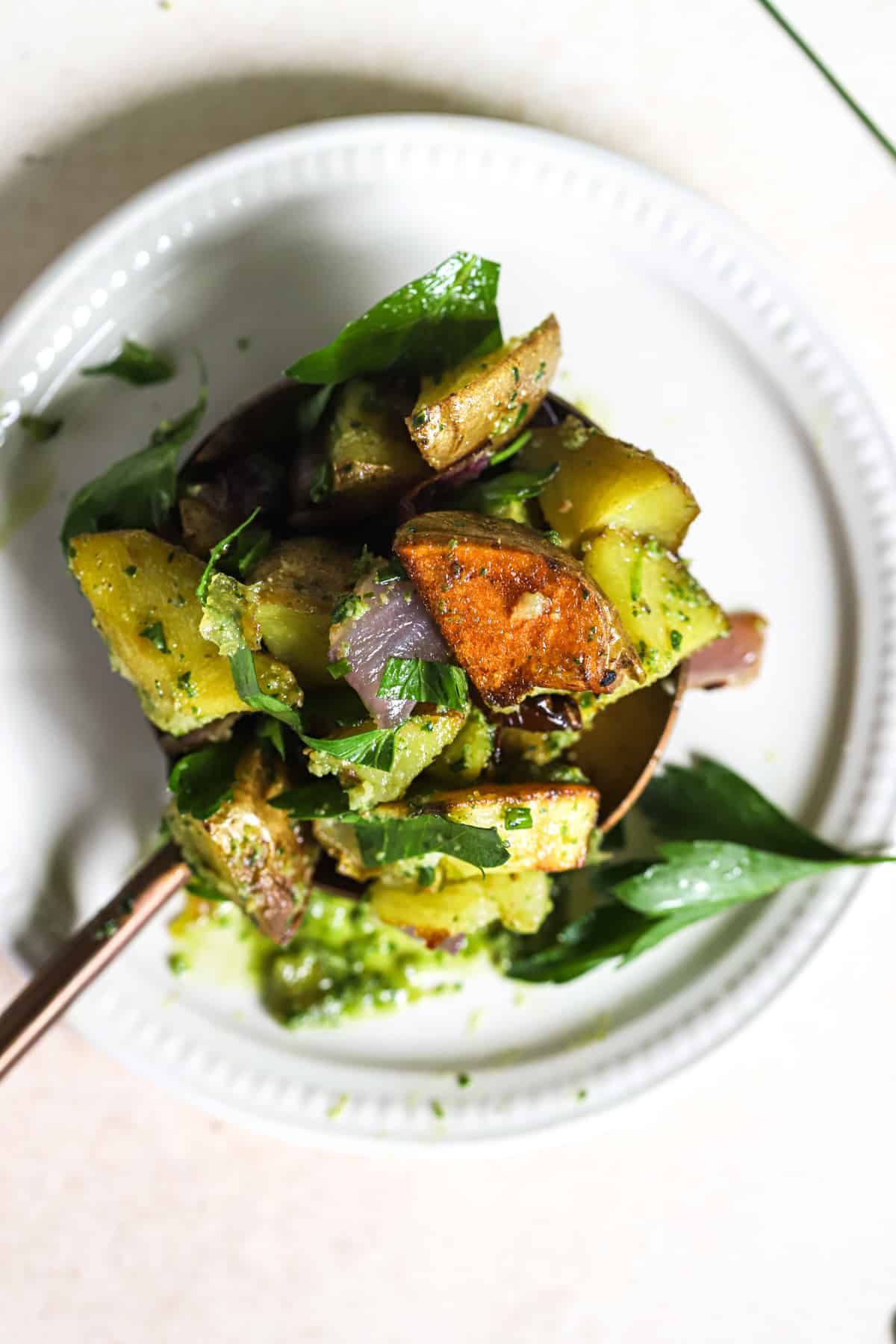 Pesto potato salad scoop on large copper spoon on small white plate, on beige and white surface