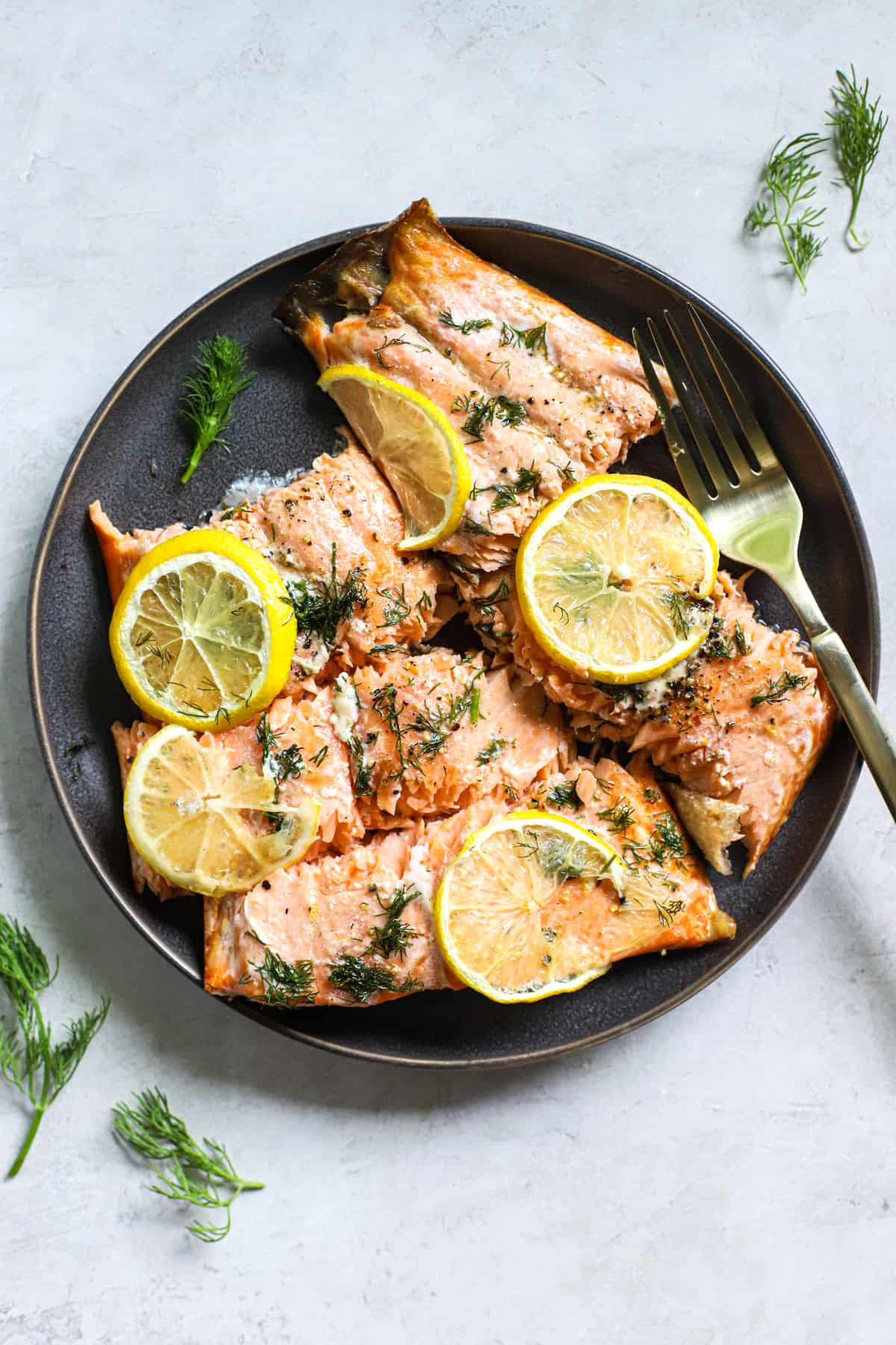 Lemon dill salmon pieces topped with lemon slices, on dark gray plate with fork