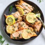 Lemon dill salmon pieces topped with lemon slices, on dark gray plate with fork