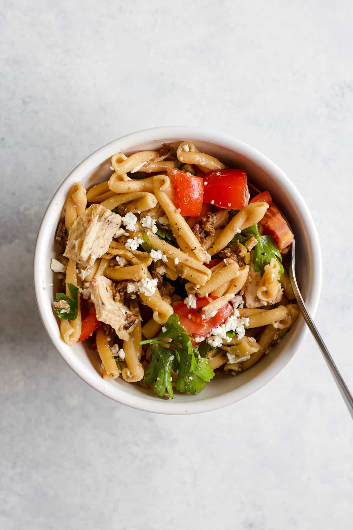 Olive tapenade and tuna pasta salad in small white bowl with fork on light blue and white surface