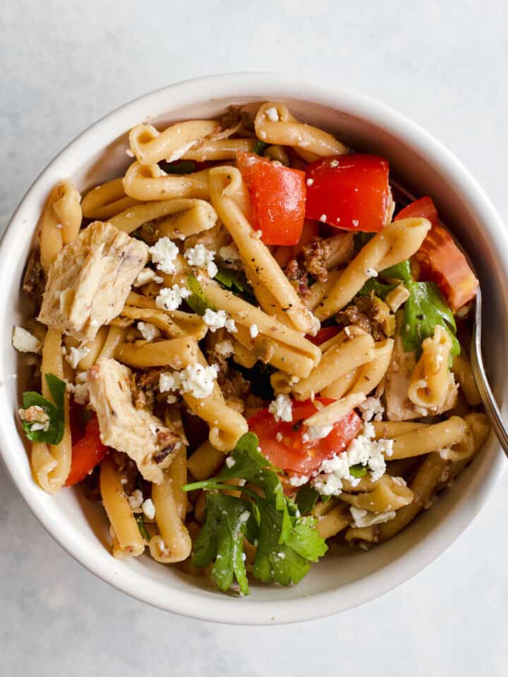 Olive tapenade and tuna pasta salad in small white bowl with fork on light blue and white surface