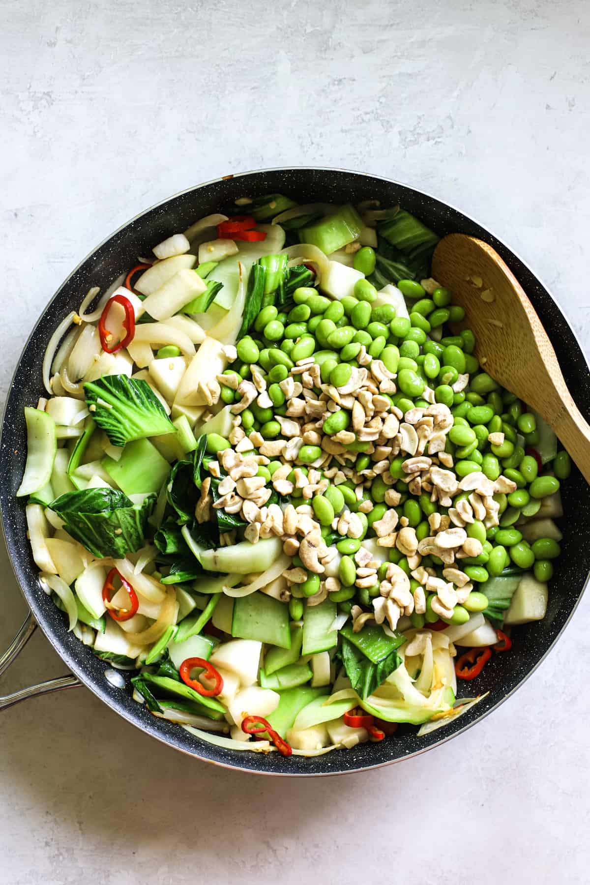 Pad pak veggies with edamame and cashes just added into sauté pan, with bamboo spoon