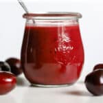 Cherry vinaigrette in small glass jar with spoon, on white marble stand with a few cherries