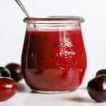 Cherry vinaigrette in small glass jar with spoon, on white marble stand with a few cherries.