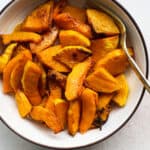 Air fryer butternut squash in beige bowl with gold spoon, on light beige and white surface