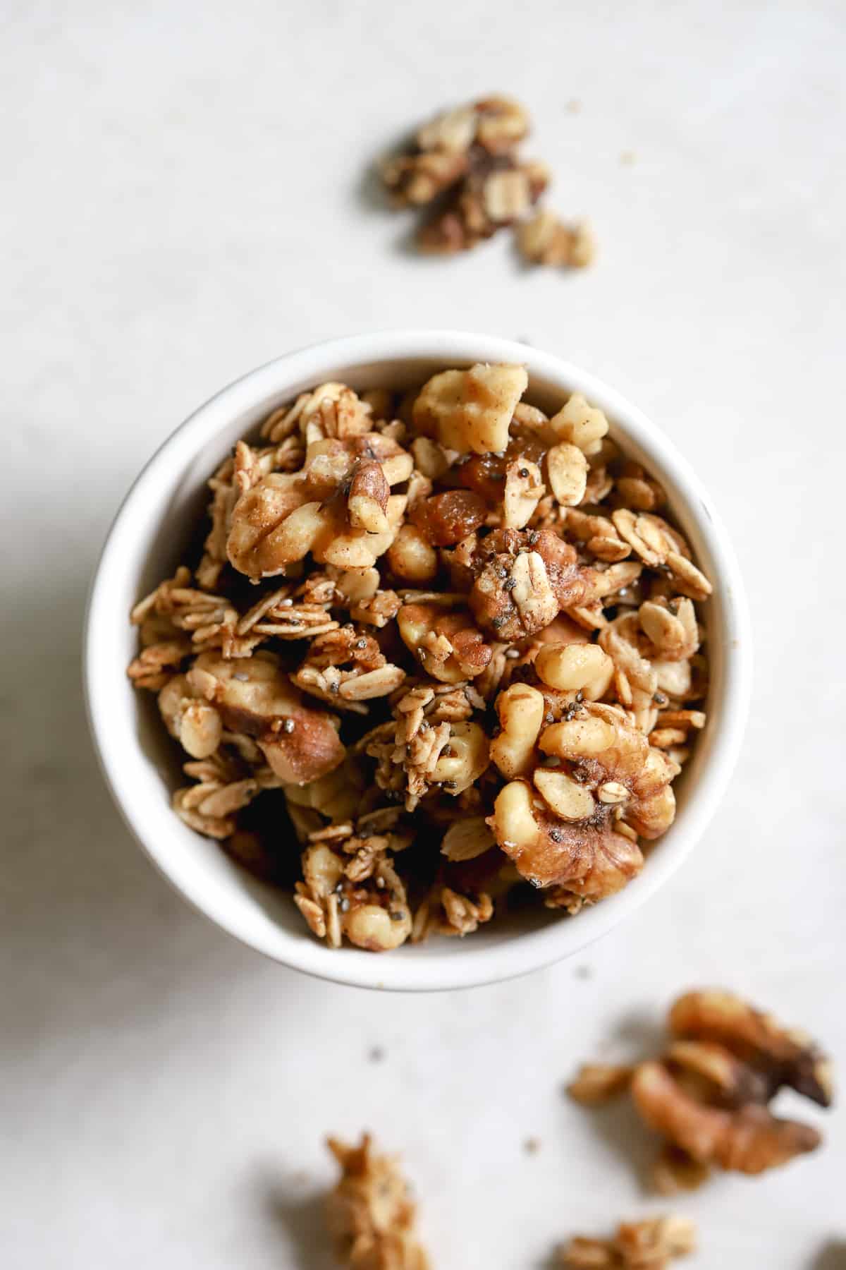 Maple cinnamon walnut granola in small white bowl on gray/with surface with a few granola pieces on the side