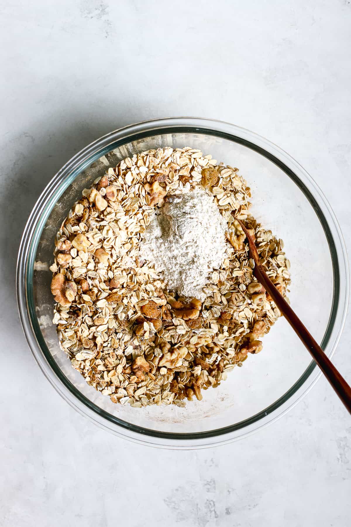 Dry granola ingredients plus white whole wheat flour in clear glass bowl on gray/white surface