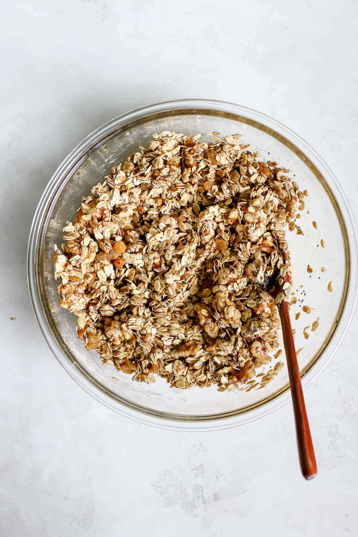 All granola ingredients mixed together in clear glass bowl on gray/white surface