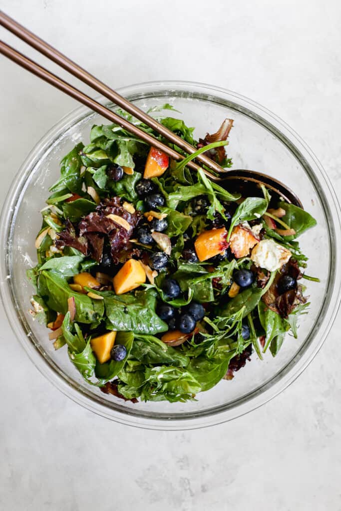 Tossing blueberry peach salad together in a bowl.
