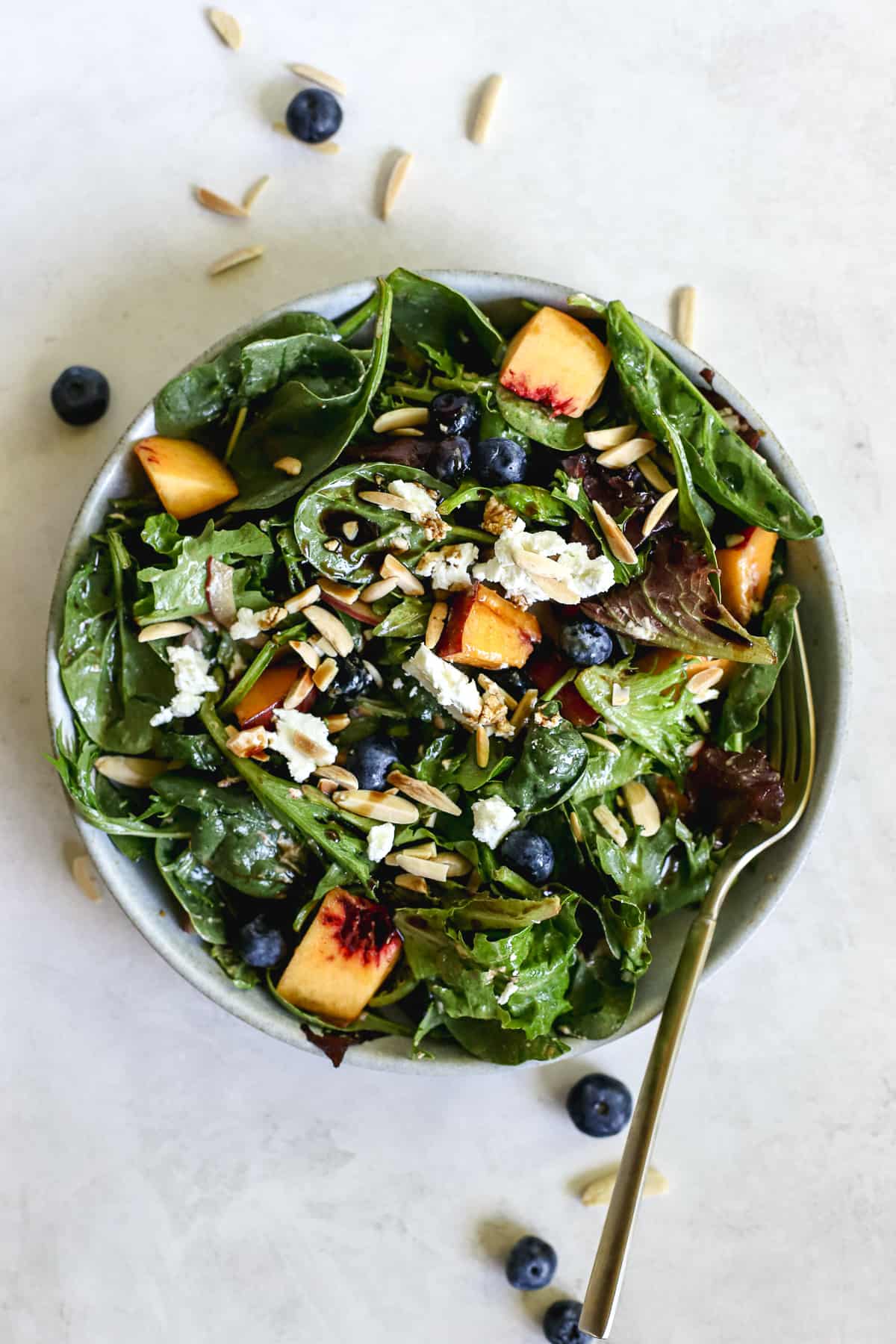 Peach blueberry salad in light blue bowl with golden fork, on light blue and white surface