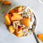 Peach pie overnight oats in small white bowl with diced fresh peaches, slivered almonds, and a dusting of cinnamon