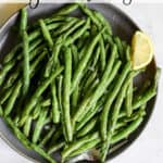 Air fryer green beans on gray plate with lemon wedges, on gray and white surface