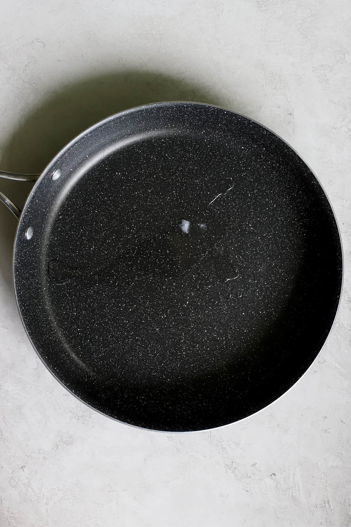 Coconut oil is melting in a black sauté pan on a gray and white surface.