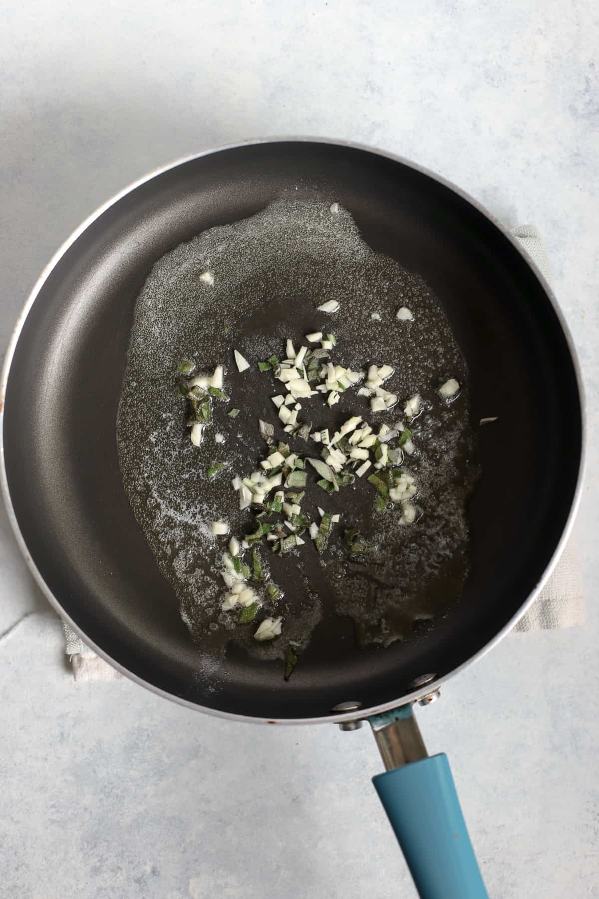 Garlic and sage sautéed in butter in skillet on light blue and white surface