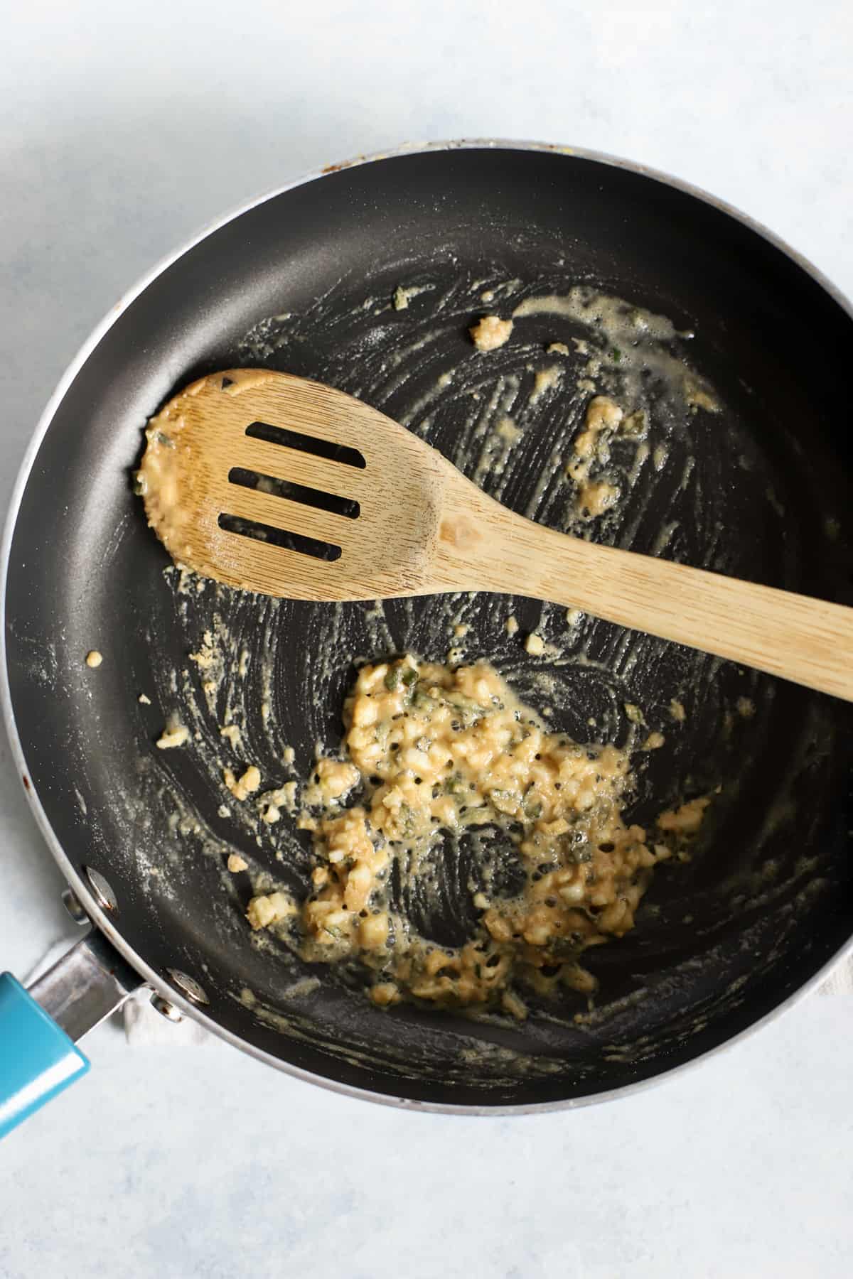Roux with butter, garlic, sage, and flour in skillet with wooden spoon, on light blue and white surface
