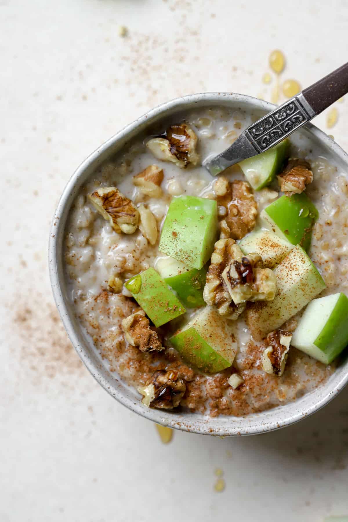 Steel cut oats in a small bowl with green apple chunks, walnuts, cinnamon, and maple syrup drizzled over the top