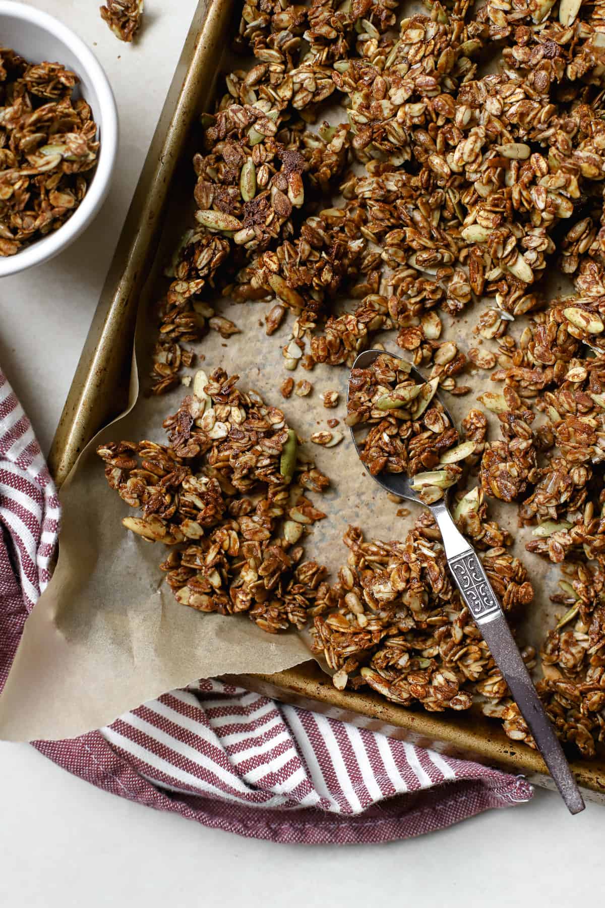 Ginger molasses granola crumbled on sheet pan lined with parchment paper, with spoon scooping some granola