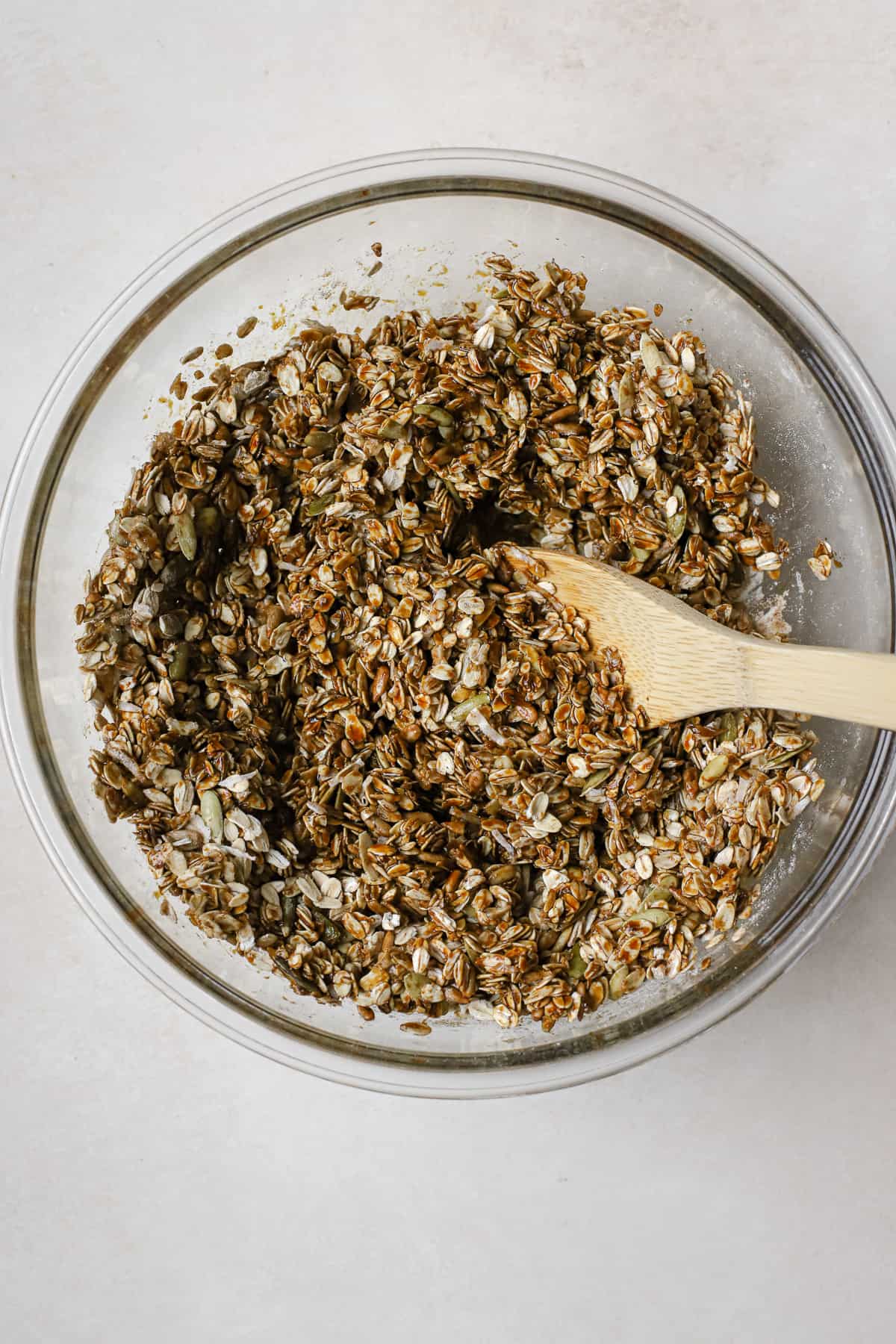 Granola mixture in clear glass bowl being stirred with a bamboo spoon