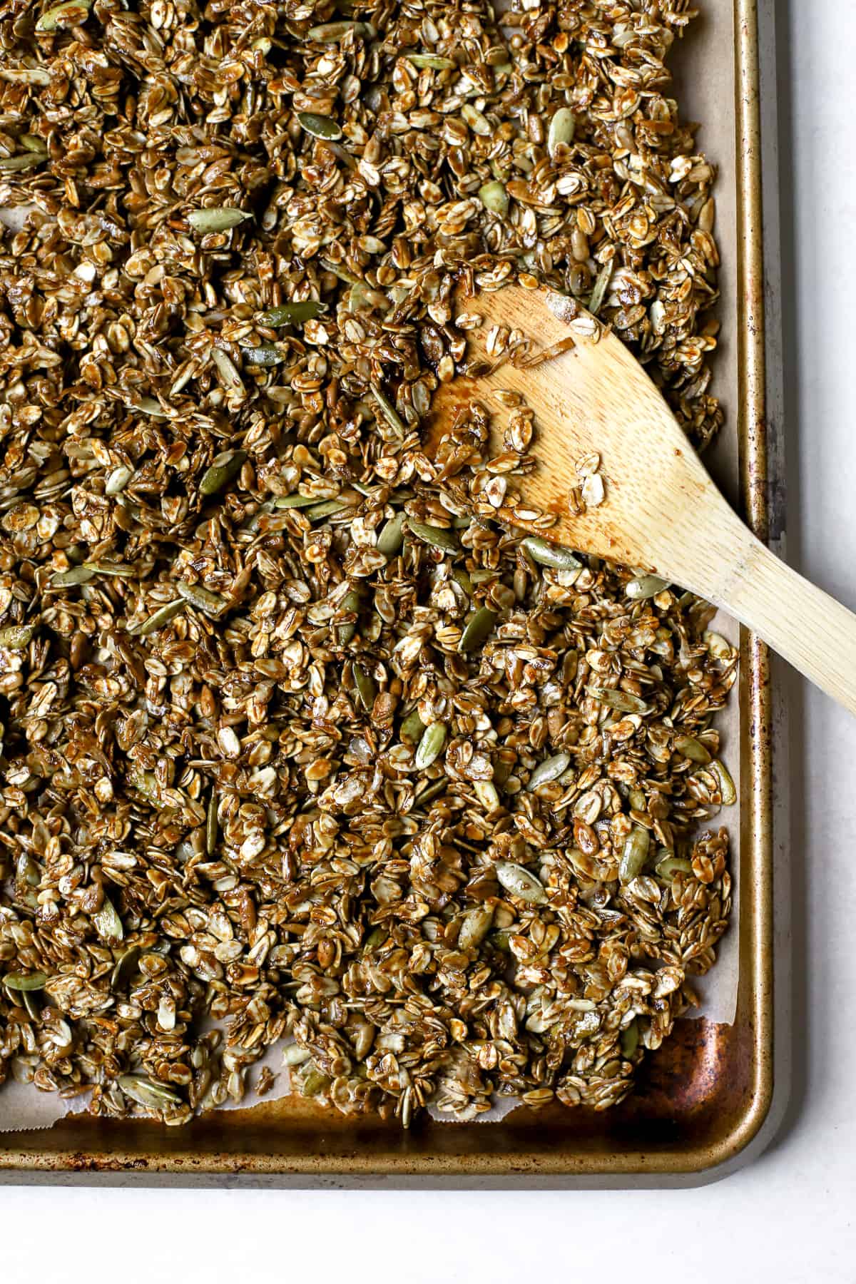 Ginger molasses granola on sheet pan lined with parchment paper and wooden spoon resting on granola