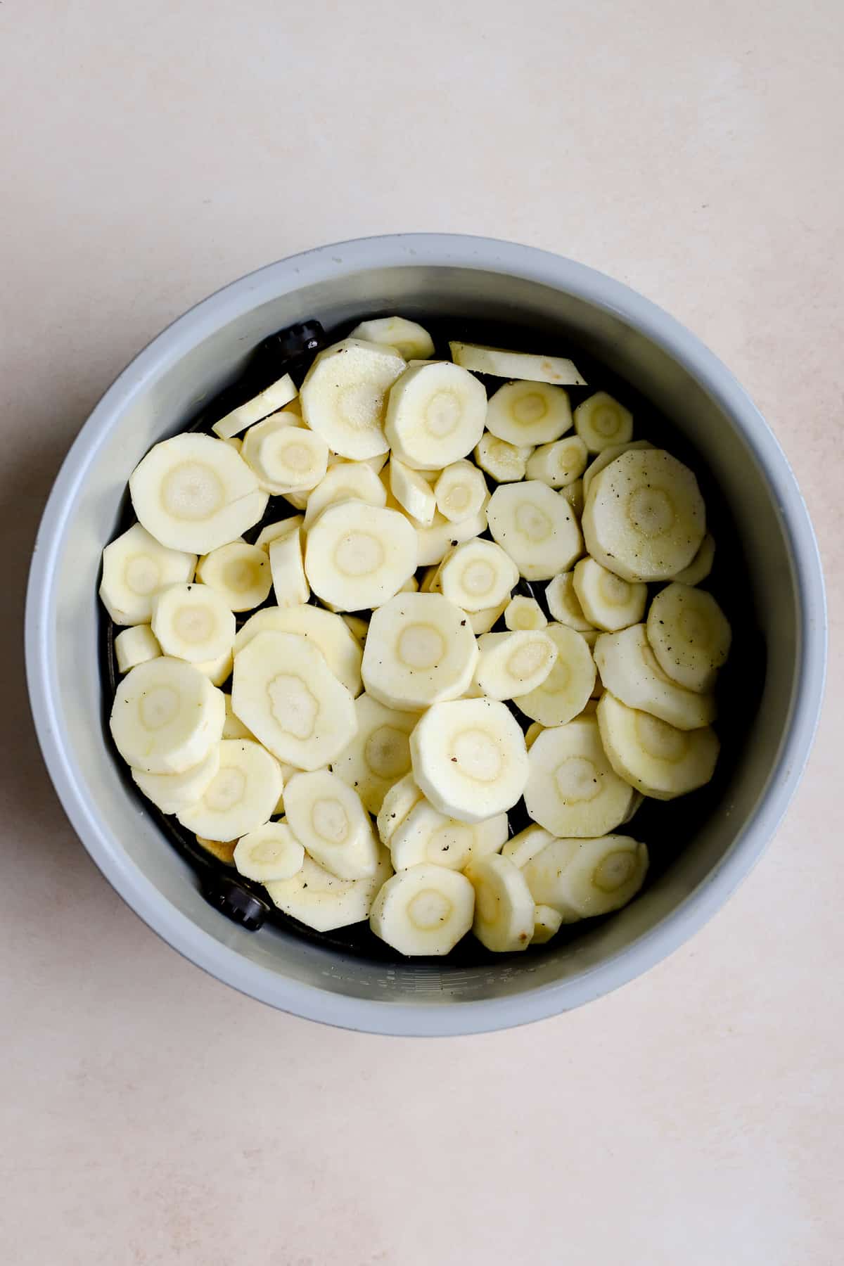 Sliced and seasoned parsnips in round air fryer basket.