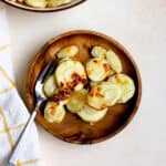 Air fryer parsnips on small wooden plate with fork topped with chili crunch and flaky salt, and other air fryer parsnips in beige serving bowl on the side