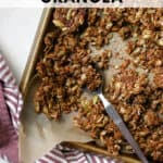 Ginger molasses granola crumbled on sheet pan lined with parchment paper, with spoon scooping some granola