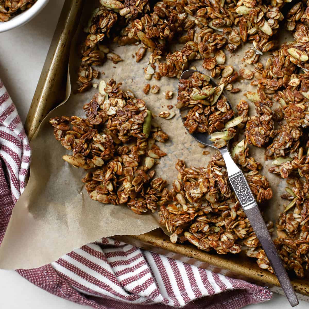 Ginger molasses granola crumbled on sheet pan lined with parchment paper with spoon