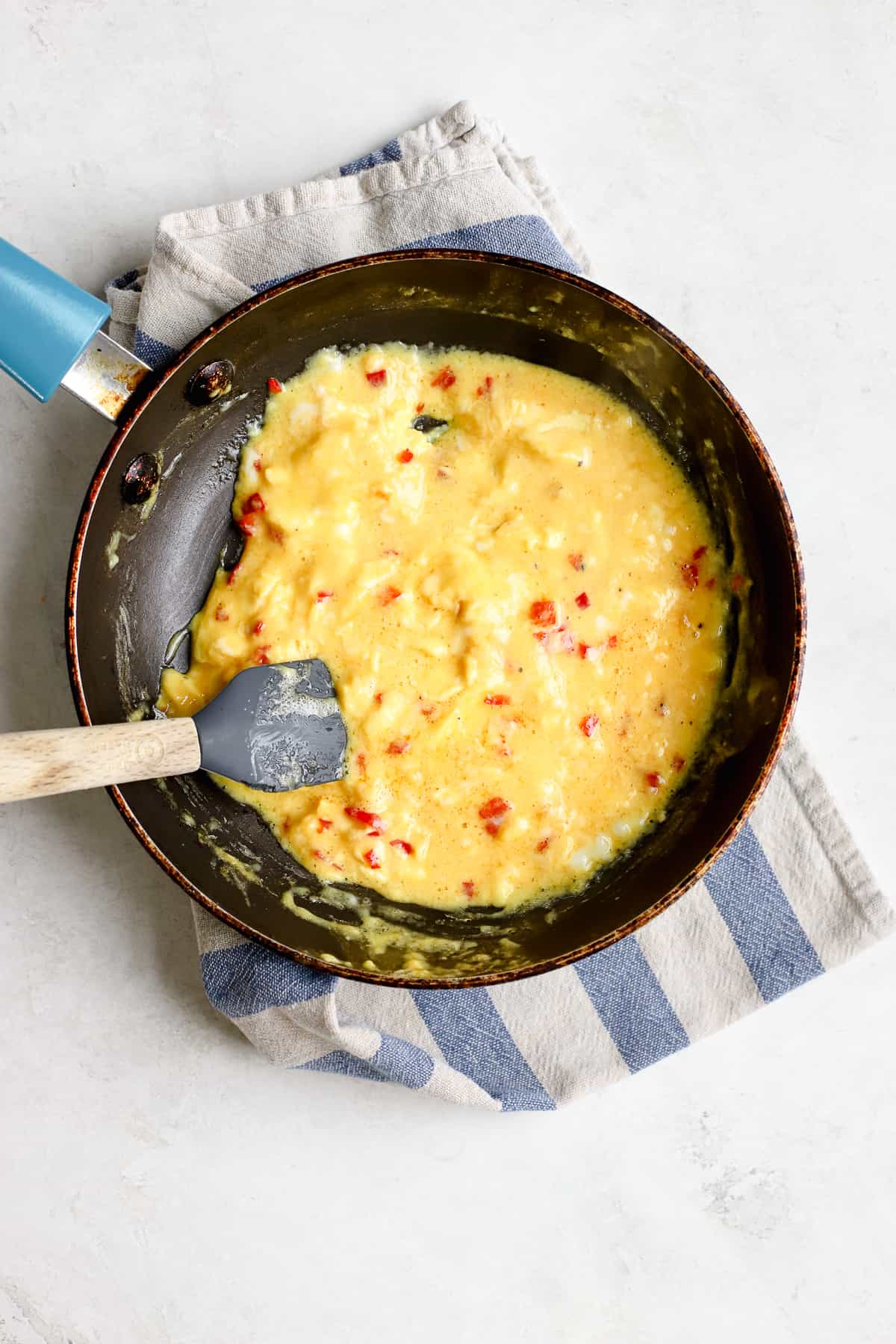 Eggs starting to scramble in small blue sauté pan with mini rubber spatula.