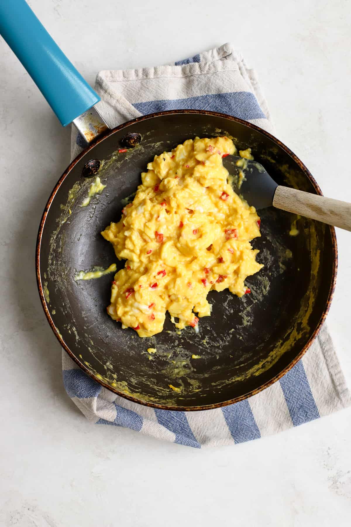 Soft, creamy chilli scrambled eggs in small blue sauté pan on blue and white striped towel on light gray surface.