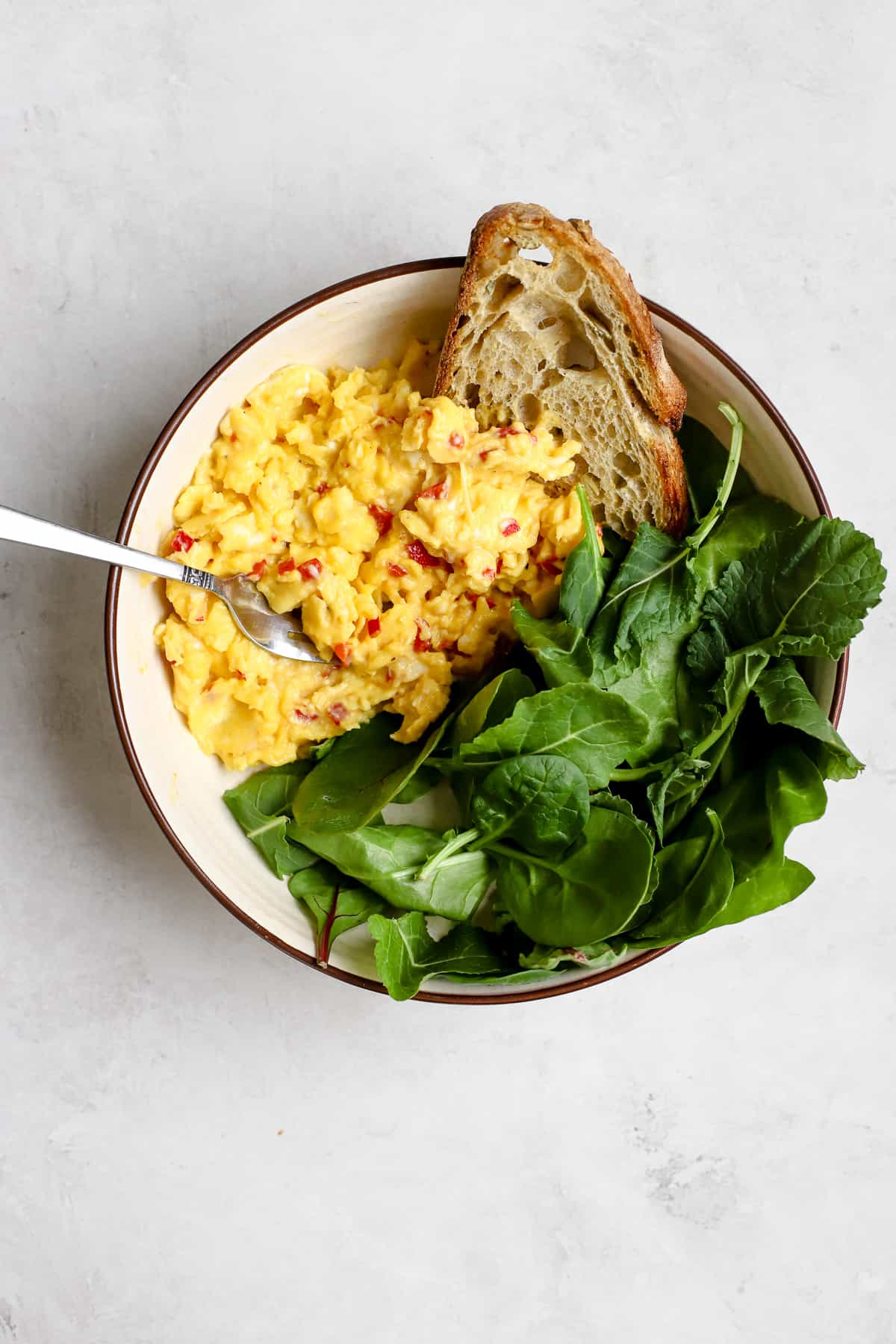 Chilli scrambled eggs in bowl with sourdough toast and greens.