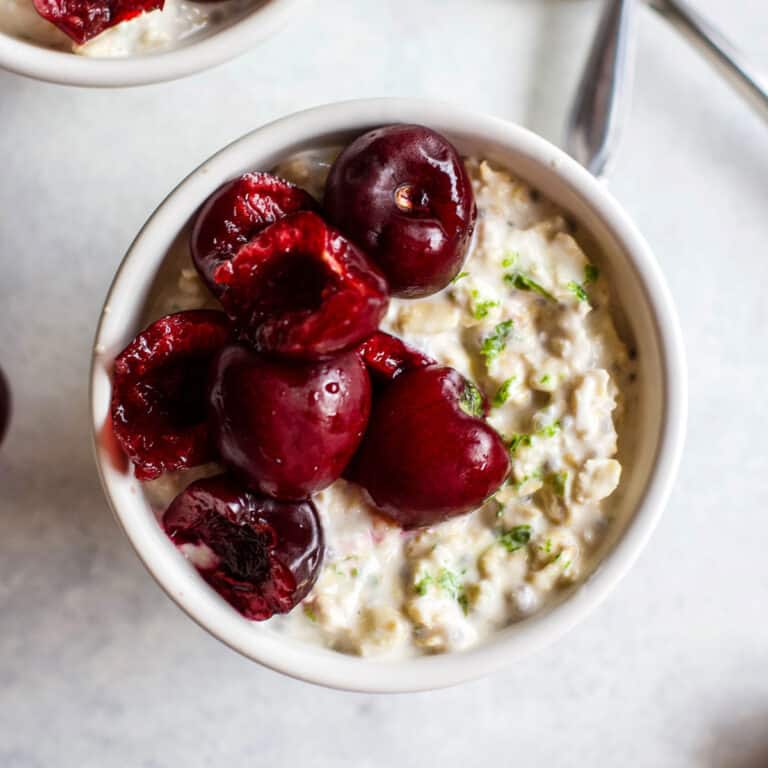 Cherry lime overnight oats in small white bowl with sweet cherries and lime zest on top, on light blue and white background