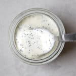 Tangy poppy seed dressing in small glass jar with spoon on gray and white surface