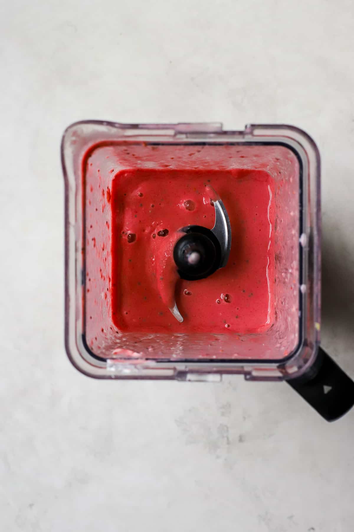 Raspberry mango smoothie blended up in a square blender on a gray and white surface.