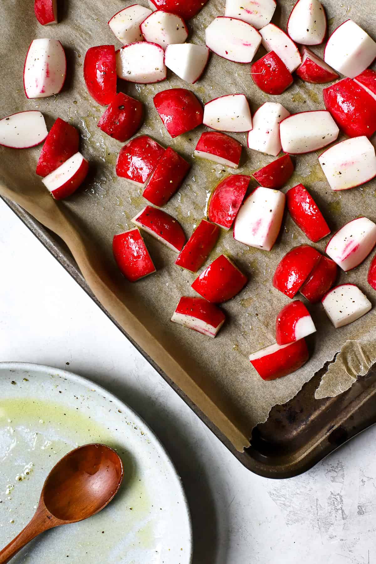 Seasoned red radishes on sheet pan before roasting.