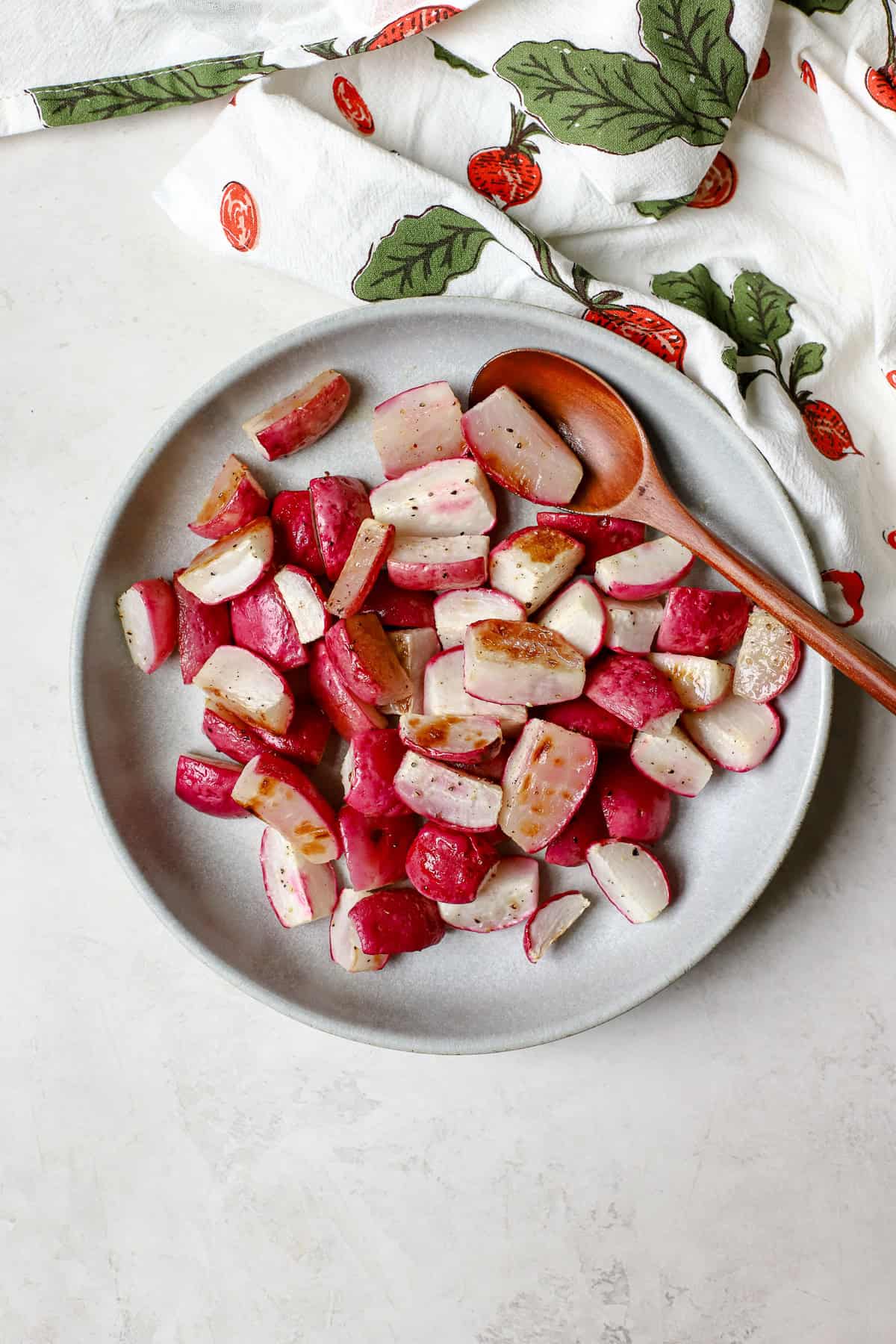 Roasted radishes in blue bowl with serving spoon.