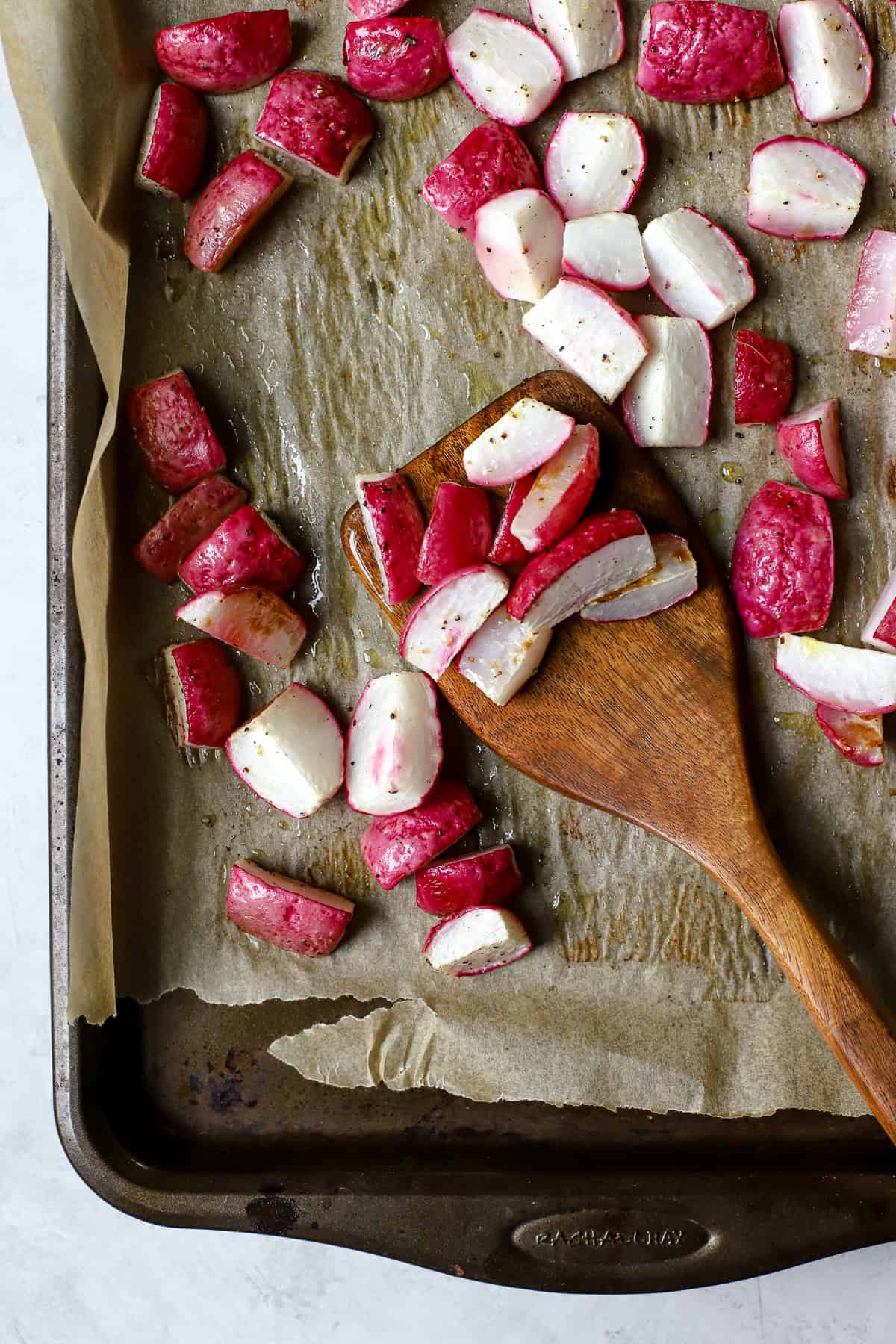 Roasted radishes on sheet pan with wooden spatula.